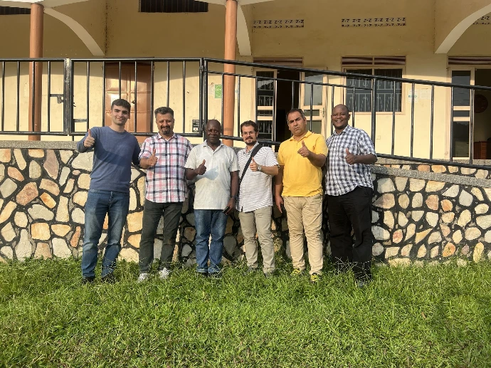 A group picture of 6 people holding a thumbs up on grass and building in the background